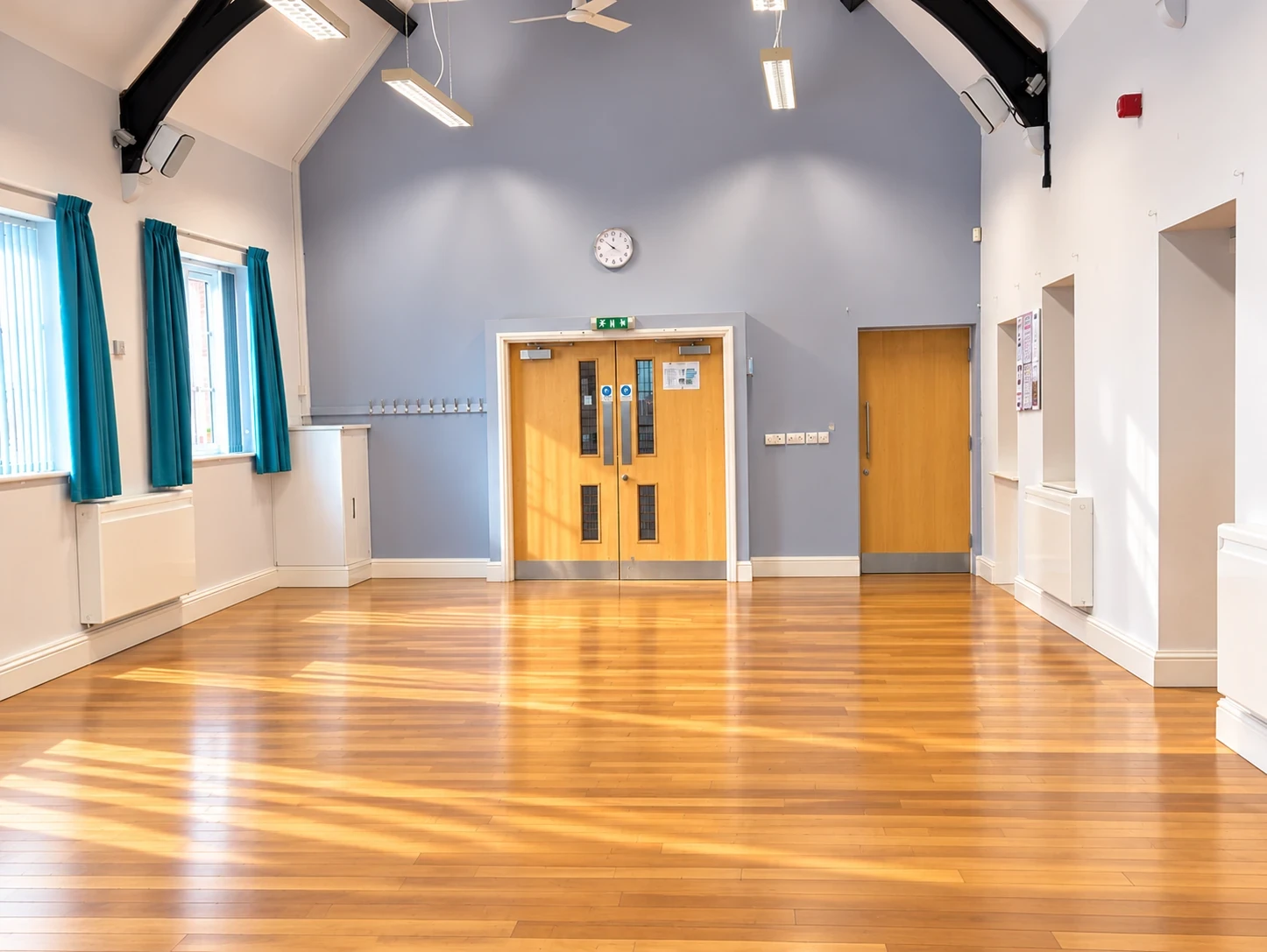 A bright, empty village hall with a wooden floor, ready for a class