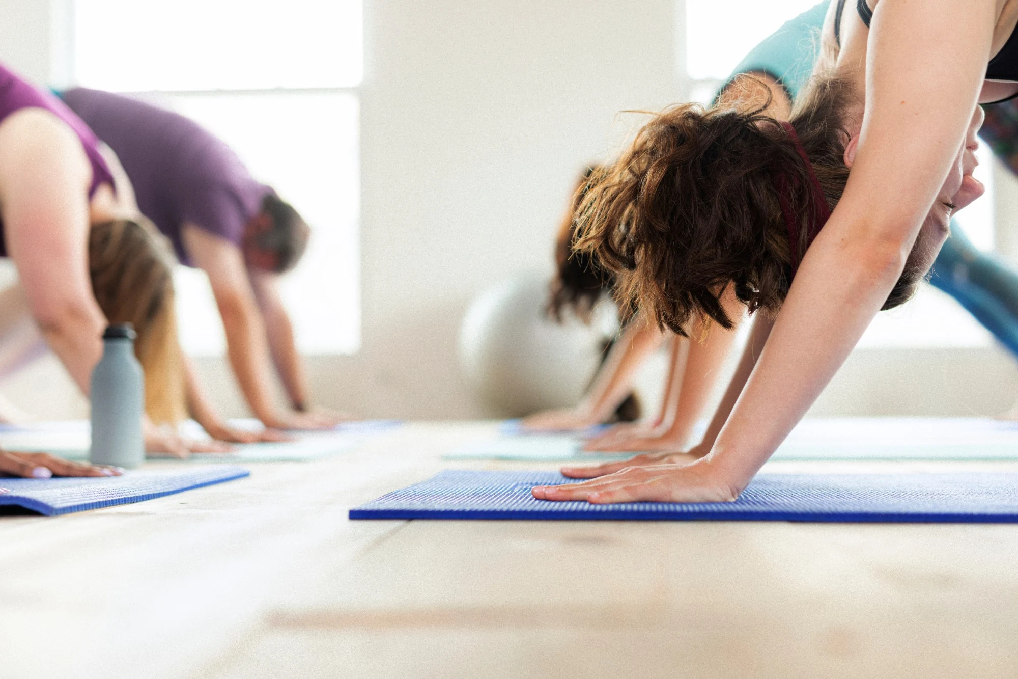 A class stretching forward on blue mats in a bright room