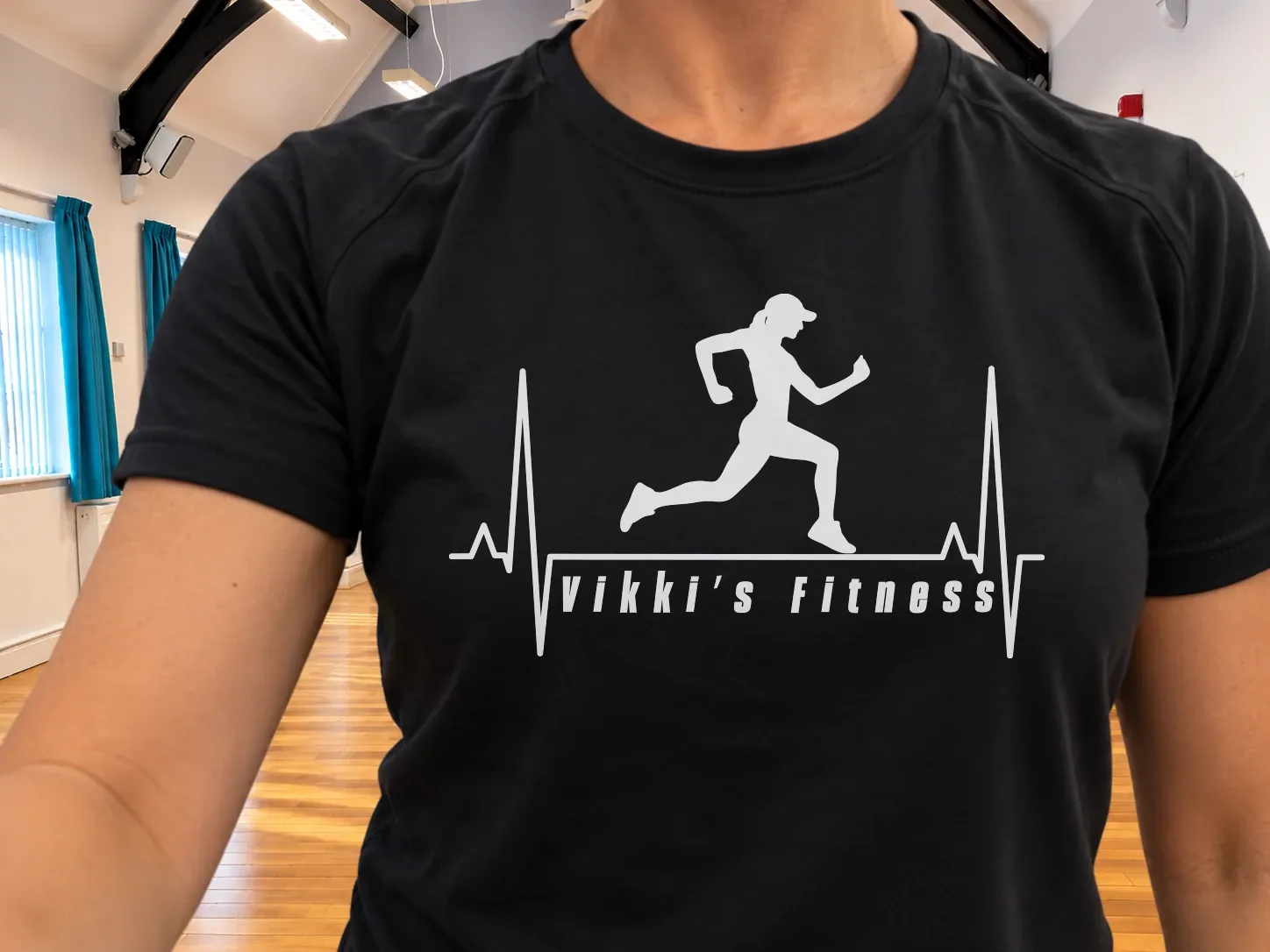 The Vikki’s Fitness logo, a runner over a heartbeat line, on a black class T-shirt